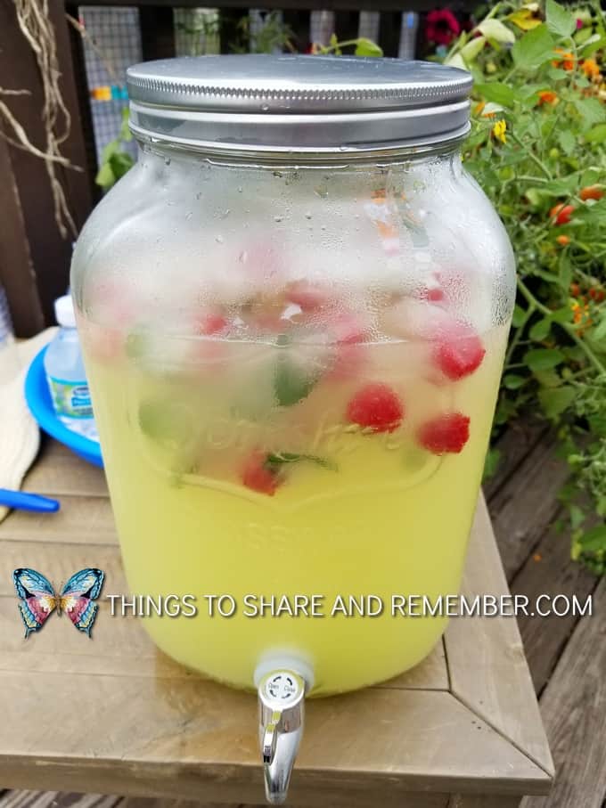 lemonade in drink dispenser with raspberries and mint