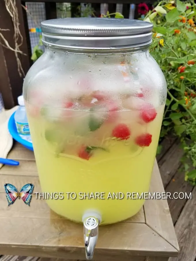 lemonade in drink dispenser with raspberries and mint