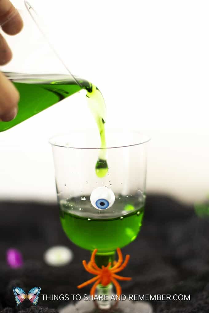 Green drink in plastic cup decorated with googly eyes and orange plastic spider for Halloween party