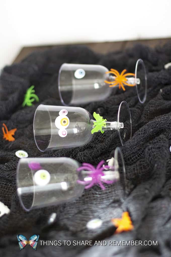 3 plastic wine cups laying on black fabric decorated for Halloween