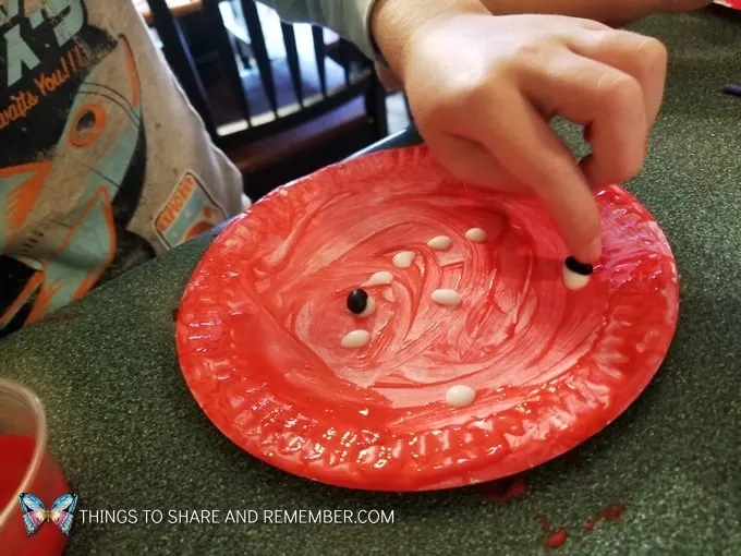 Apple Seed Art gluing seeds on a red painted paper plate