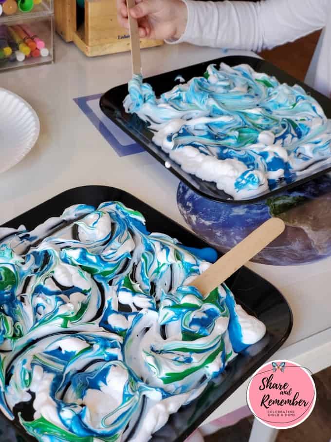 Swirling green and blue paint in shaving cream with a craft stick.