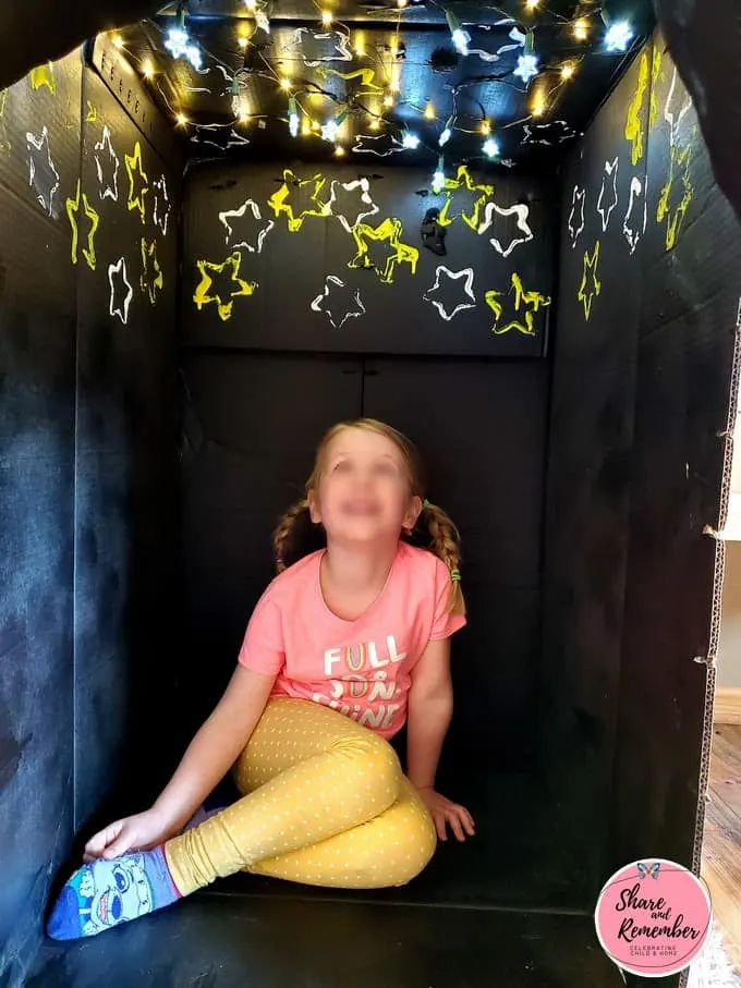 Child looking at lights and stars in black Cardboard Box Planetarium.