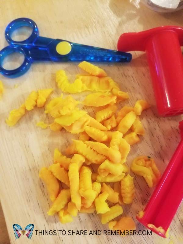 yellow playdough pieces made with red playdough extruder and blue plastic scissors