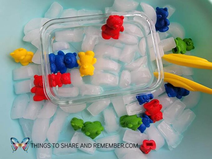 blue tray with glass dish of water, teddy bear counters, ice cubes and tweezers create a toddler sensory bin